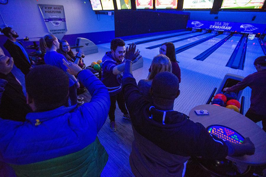 Student gather in the bowling alley with the black lights on.